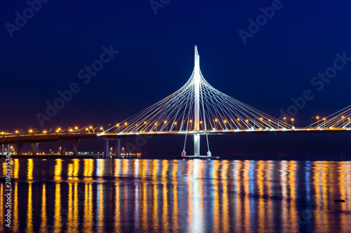 Cable-stayed bridge connects the roads of Western high-speed diameter in St. Petersburg, Russia. Night lighting of bridge is reflected in water of Peter's fairway. Modern industrial road structures