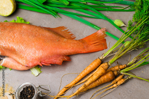 red sea perch on the table with young carrot, spices, lime, green onion photo