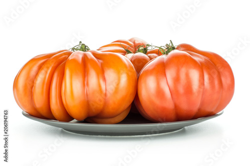Three beef tomatoes on a grey ceramic plate isolated on white background big ripe red ribbing.
