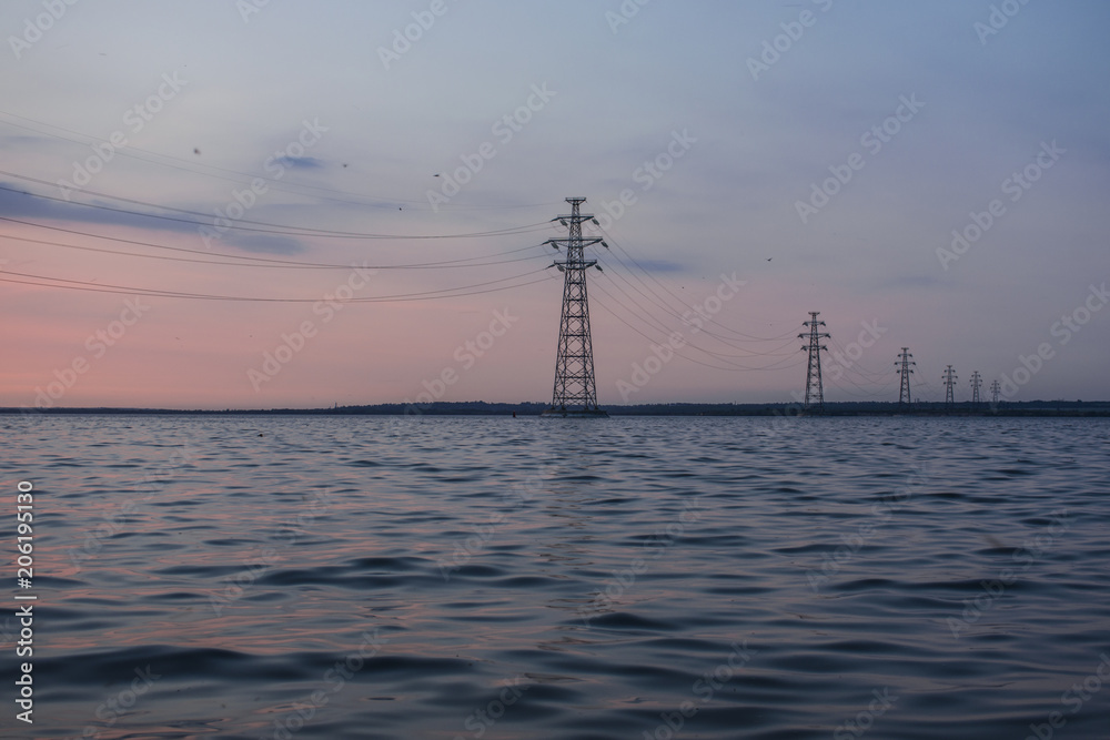 Power lines against a beautiful sunset on the water. The country's industry is a source of heat and light