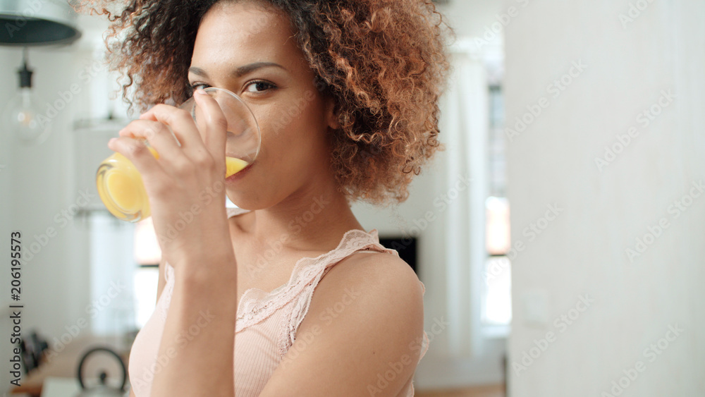 Happy mixed race woman holding orange juice in a kitchen. Happy mixed race woman holding orange juice in a kitchen.