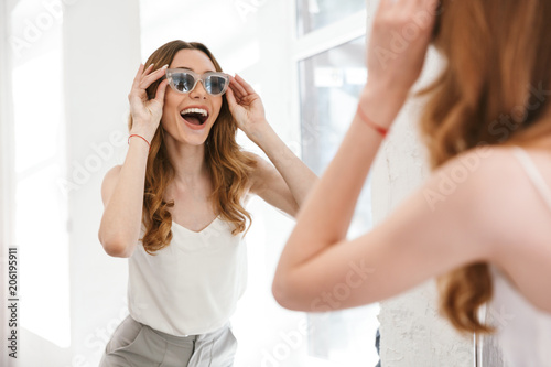 Obraz na plátne Cheerful young woman trying on new sunglasses