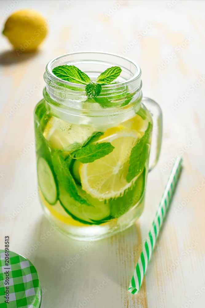 Fototapeta premium Detox water infused with sliced lemon, cucumber and sprigs of mint on wooden background.