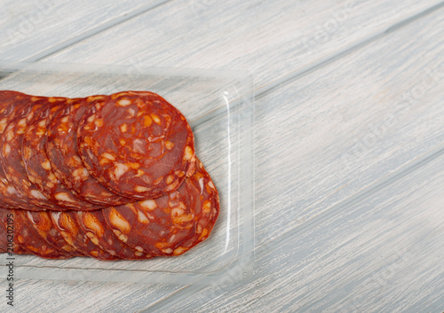Chorizo made with pork in plastic container on wooden table. Copy space.