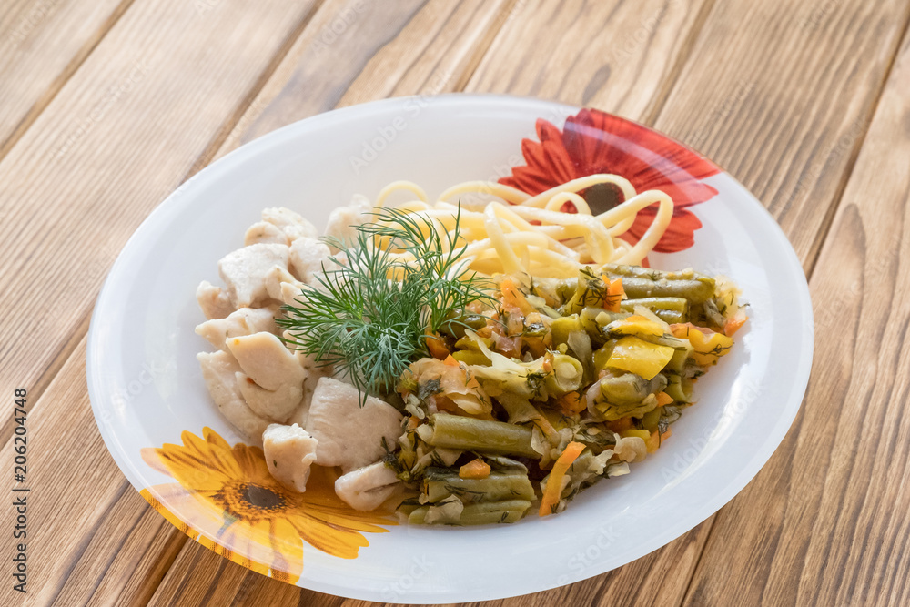 Chicken meat in a plate with fried vegetables and pasta. Portioned lunch on wooden background