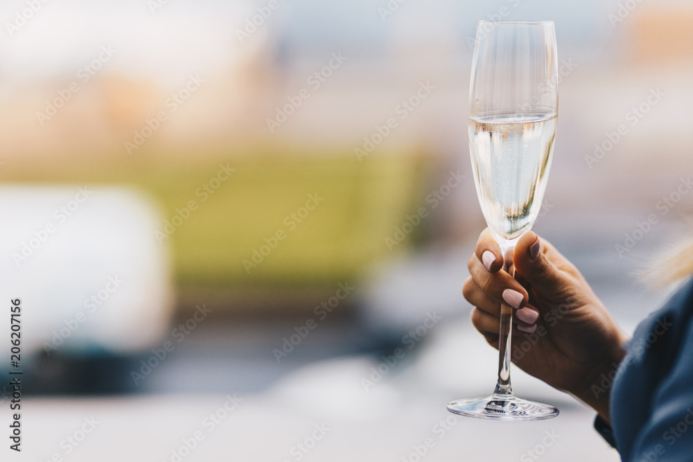 Unrecognizable female with gentle manicure holds glass of sparkle white wine or champagne against blurred background. People, leisure and drinking concept