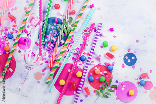 Party concept with bar supplies, colorful flat lay with copy space. Tall cocktail glass with straws, candies, sweets and confetti.