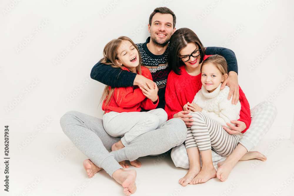Family relationship concept. Cute cheerful little small girl have fun and enjoy spare time with their parents. Happy male father embraces his wife and daughters, feels delighted, isolated on white Family relationship concept. Cute cheerful little small girl have fun and enjoy spare time with their parents. Happy male father embraces his wife and daughters, feels delighted, isolated on white