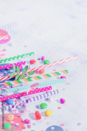Cocktail straws, confetti and candies close-up in a colorful party supplies concept on a light background with copy space. Holiday accessories