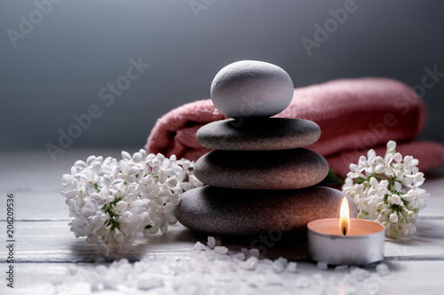 Spa still life with stack of stones burning candle  sea salt  towel and white flowers on white wooden table