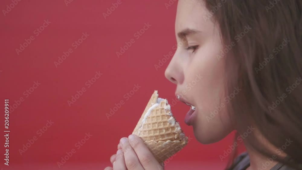 Pretty baby girl kid eating slow motion video nursing bottle licking big ice cream in waffle cone lifestyle with raspberry happy laughing on red background. the girl teenager and ice cream concept