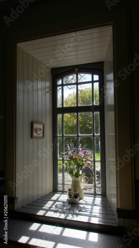 Colourful wildflowers in a cream jug on the wooden windowsill of a picturesque framed window.