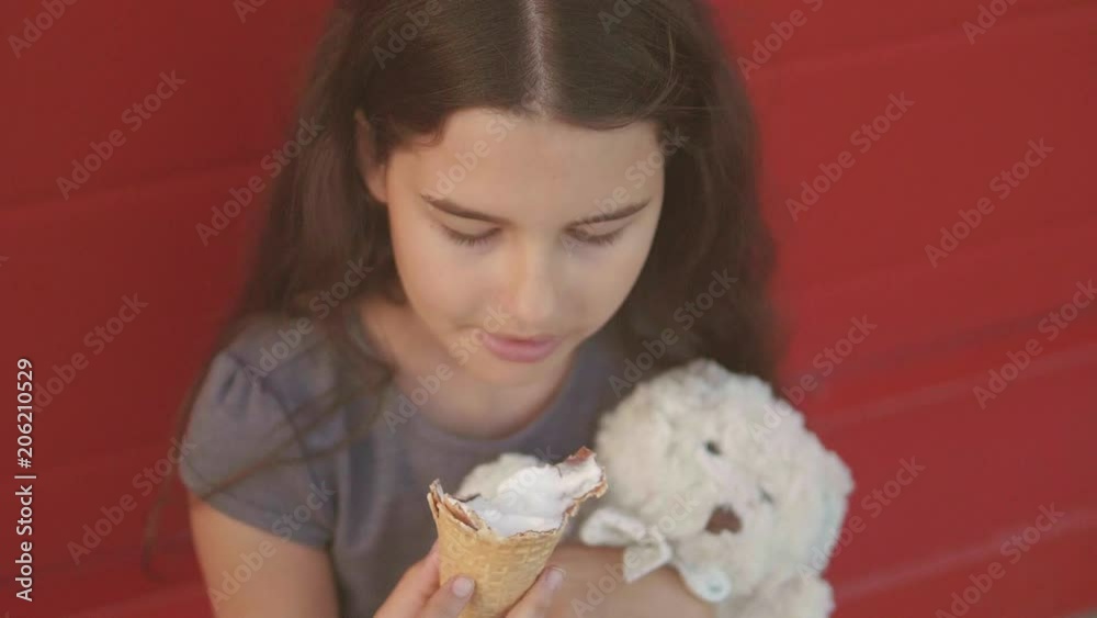 Pretty baby girl kid eating slow motion lifestyle video nursing bottle licking big ice cream in waffle cone with raspberry happy laughing on red background. the girl teenager and ice cream concept Pretty baby girl kid eating slow motion lifestyle video nursing bottle licking big ice cream in waffle cone with raspberry happy laughing on red background. the girl teenager and ice cream concept