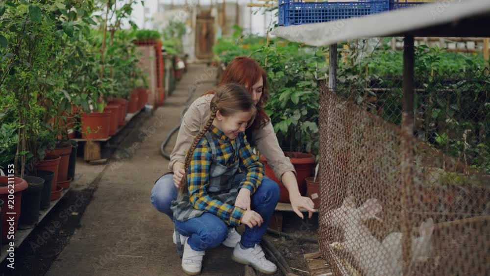 Greenhouse worker and her excited daughter are playing with rabbits in