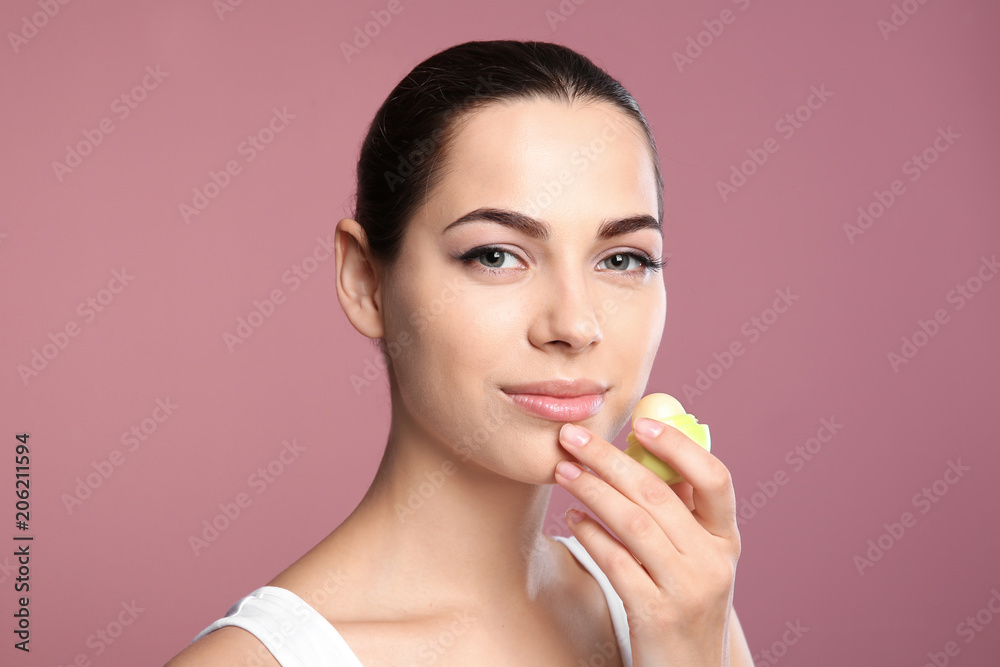 Young woman applying balm on her lips against color background Young woman applying balm on her lips against color background
