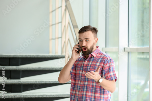 Portrait of handsome bearded man with mobile phone near stairs, indoors