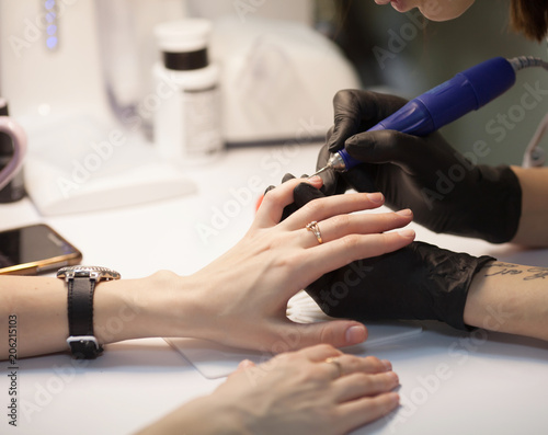 Manicure in process.Closeup shot of a woman in a nail salon receiving a manicure by a beautician with nail file. Woman getting nail manicure. Beautician file nails to a customer.