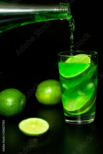 Glass of cold drink with ice and fresh ripe slice green limes on black