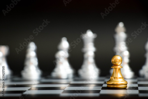 Gold pawn in chess game face with the another silver team on black background (Concept for company strategy, business victory or decision)