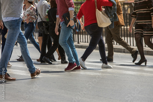 People stranded and distracted crossing the street in the pedestrian crossing at a busy intersection crowded and crowded in the midst of traffic only showing up the legs and feet. Walking and talking 