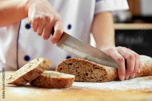 Close up of female baker with knife cutting fresh grain bread. Organic food concept. 
