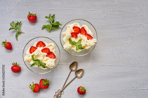 Homemade summer dessert with sliced strawberries and cream cheese in the glass bowls on a gray background with copy space. Decorated with vintage spoons and fresh mint leaves. Top view