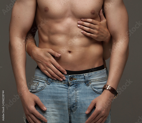 Sexy muscular naked man and female hands unbuckle his jeans on a dark background