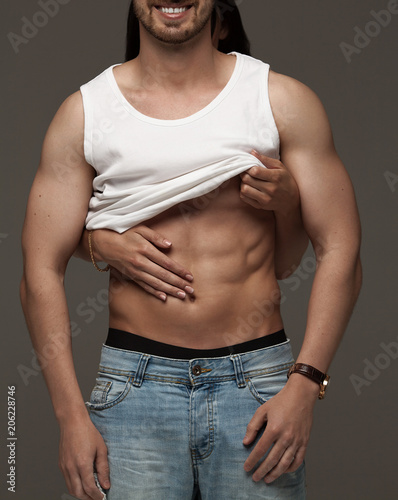 Sexy muscular naked man and female hands unbuckle his jeans on a dark background photo
