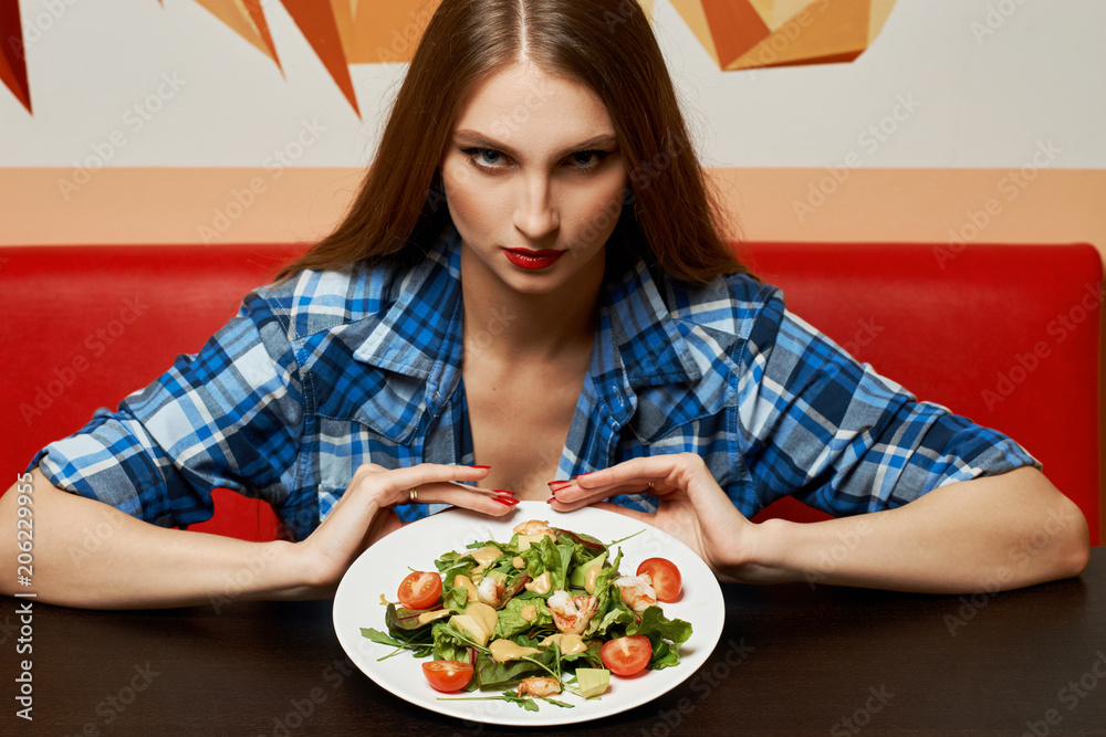 Portrait of seductive young woman dressed in checkered unbuttoned shirt holding plate with delicious vegetable salad made of shrimps, tomatoes, avocado. Sexy female model demonstrating tasty meal. Portrait of seductive young woman dressed in checkered unbuttoned shirt holding plate with delicious vegetable salad made of shrimps, tomatoes, avocado. Sexy female model demonstrating tasty meal.