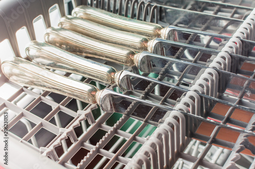 Silver table knives lie in the upper compartment of the dishwasher