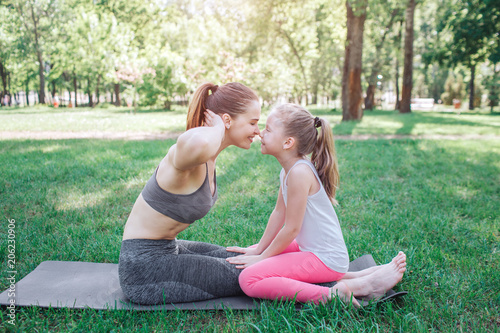 Cute picture of mom and daughter sitting together face to face. Woman is holding her hands close to head. They are touching each others noses and smiling. Yoga and Pilates Concept