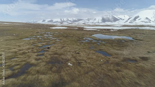 Fast Flying over Small Lakes with Ice Blocks in Spring. Snowy Mountains on Background. Aerial Low Angle View. Arabel Plateu. Kyrgyzstan photo