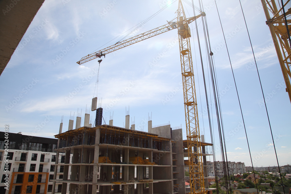 A modern new building. Working crane on the construction of the house. Construction site with cranes on sky background. 