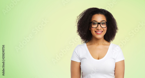 vision, body positive and people concept - happy african american woman in white t-shirt and glasses over lime green background