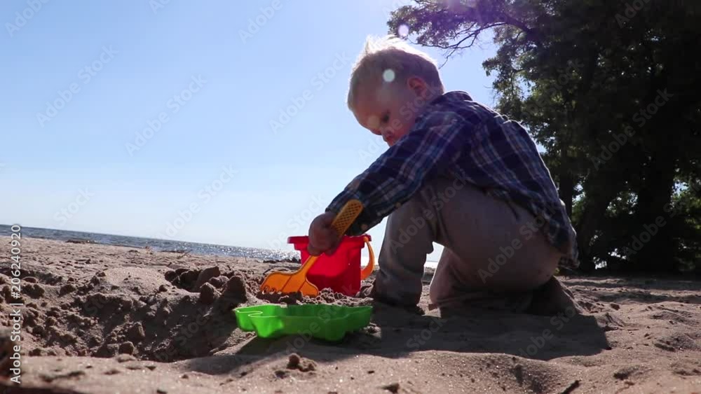 A little boy is playing in the sand on the sea, little legs and fingers, in a swimsuit, a background of sea yellow sand and blue water. Concept: children, childhood, summer, freedom, children, child.