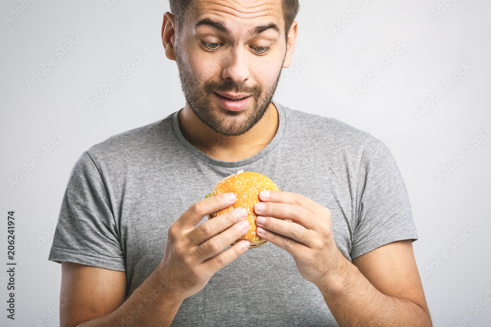 Young man holding a piece of hamburger. Student eats fast food. Burger is not helpful food. Very hungry guy. Diet concept. Young man holding a piece of hamburger. Student eats fast food. Burger is not helpful food. Very hungry guy. Diet concept.