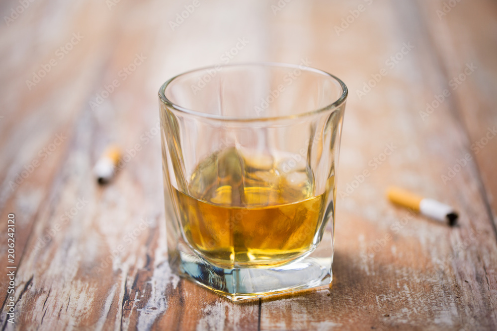 alcohol addiction and alcoholism concept - close up of glass of whiskey and cigarette butts on table alcohol addiction and alcoholism concept - close up of glass of whiskey and cigarette butts on table