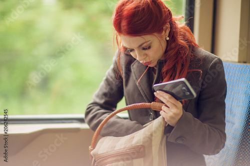 beautiful young woman in the tram, subway, train with cell phone, looking in her hand bag, purse, autumn mood colors
