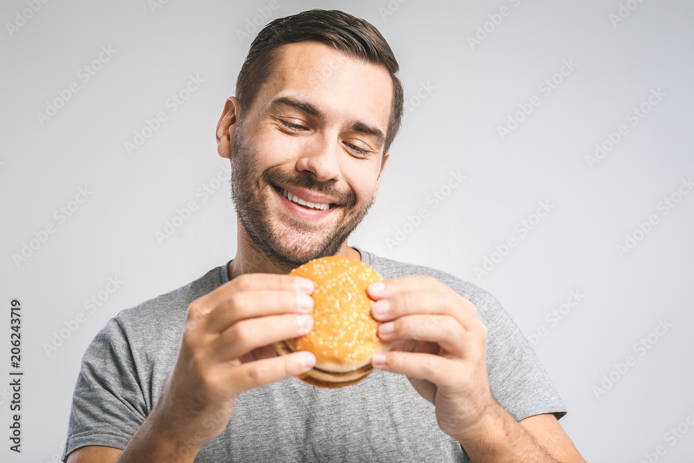 Young man holding a piece of hamburger. Student eats fast food. Burger is not helpful food. Very hungry guy. Diet concept. Young man holding a piece of hamburger. Student eats fast food. Burger is not helpful food. Very hungry guy. Diet concept.