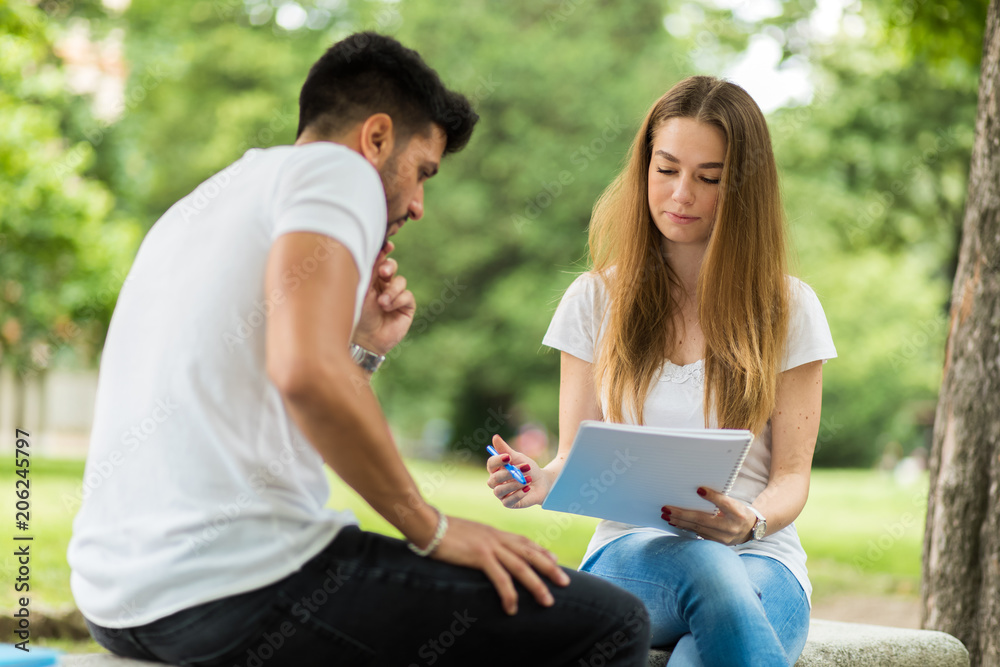 Two students studying together sitting on a bench outdoor Two students studying together sitting on a bench outdoor