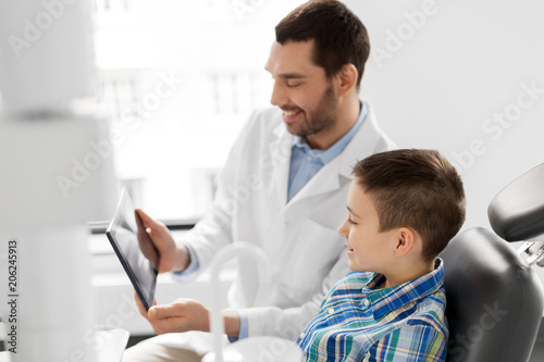 medicine  dentistry and healthcare concept - smiling male dentist showing tablet pc computer to kid patient at dental clinic