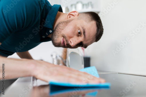 Φωτογραφία household and people concept - man wiping table with cloth cleaning cooker at ho