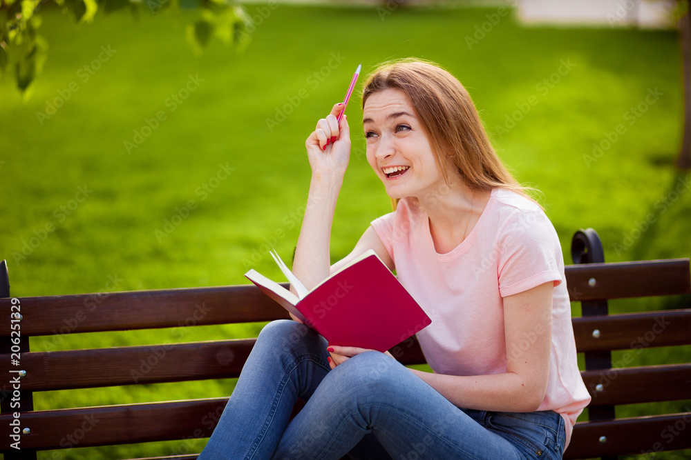 Obraz premium Girl is thinking what to write in a notebook, sitting in the Park