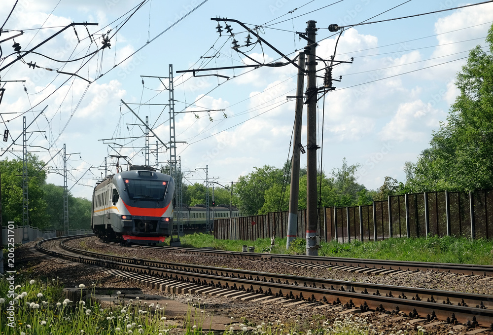 Fototapeta premium City landscape railroad track rails and passenger train moving on sunny summer day horizontal view