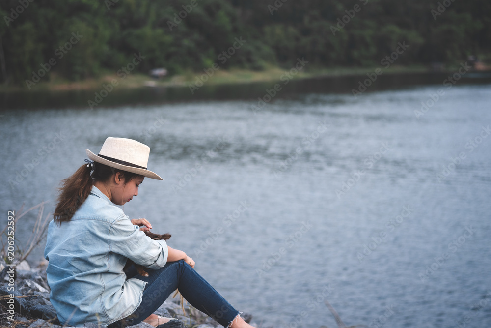 Young asian woman in hat wear denim shirt sitting with her dogs beside lake with mountain view. Young asian woman in hat wear denim shirt sitting with her dogs beside lake with mountain view.
