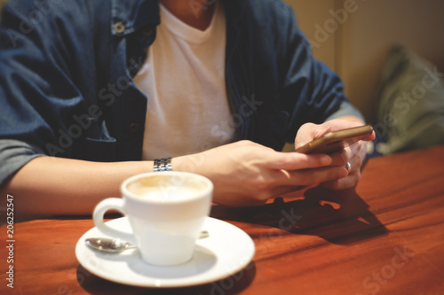 Young hipster man using smartphone with a cup of coffee in cafe in vintage tone.