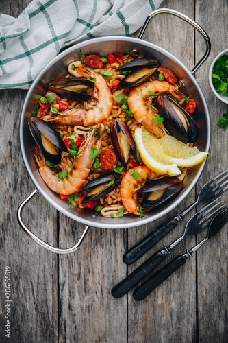 Spanish seafood paella with mussels, shrimps and chorizo sausages in traditional pan on wooden background.