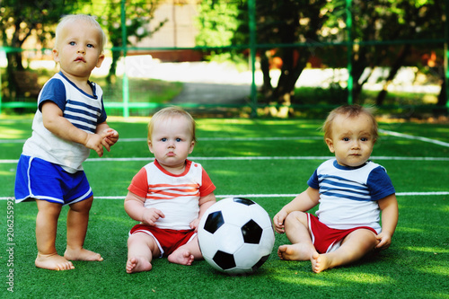 Three little kids in a sports ground with a soccer ball. Tiny football team learning to play (and to walk). Children friendship and active leisure concept