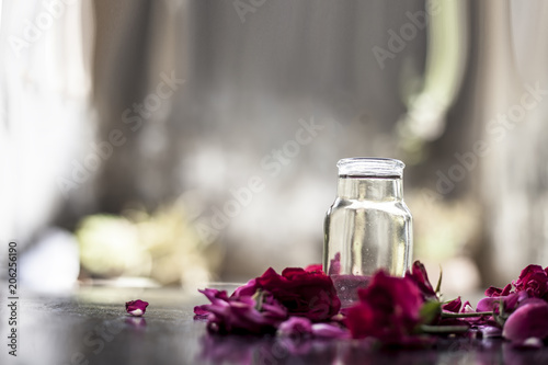 Medicinal and floral essence of Rose or gulab popularly known as gulab jal or gulab ka pani in Asia with fresh bright rose petals on wooden surface.