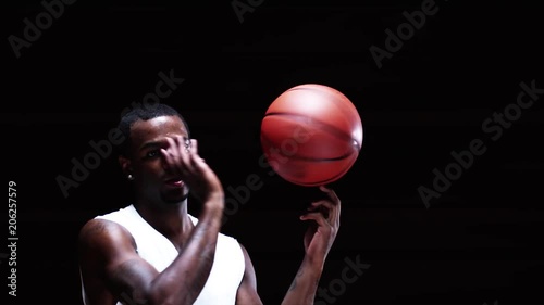 An athlete spins a basketball on his finger on a black backdrop photo